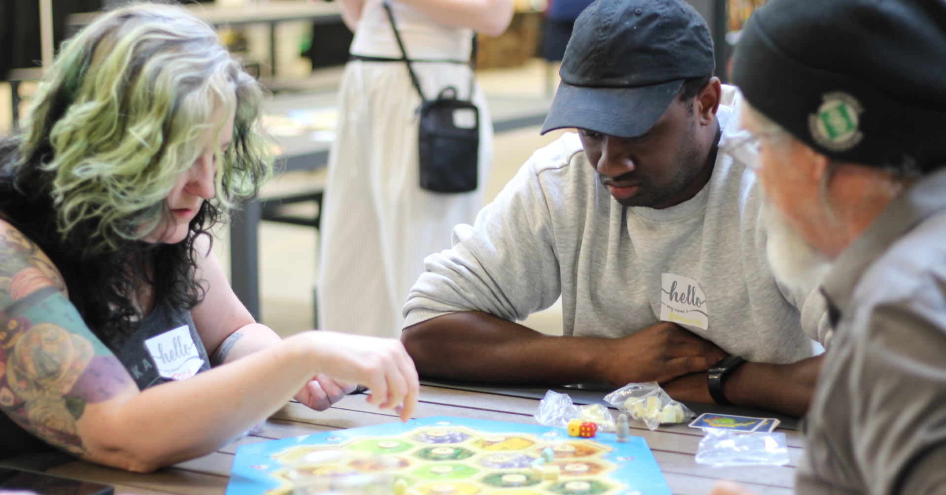 Three people playing Catan and rolling dice at a local board game group meetup in Saskatoon.