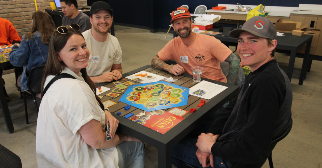 A group of four friends smiling around a Catan board during a board game night in Saskatoon.